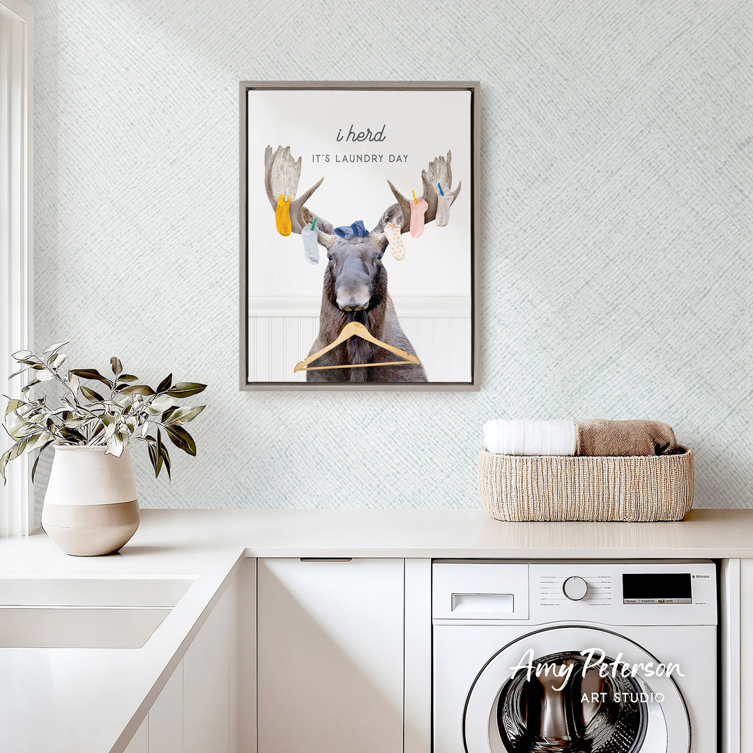 a framed poster of a moose with a laundry basket on a counter, and a potted plant on the left side of the frame.