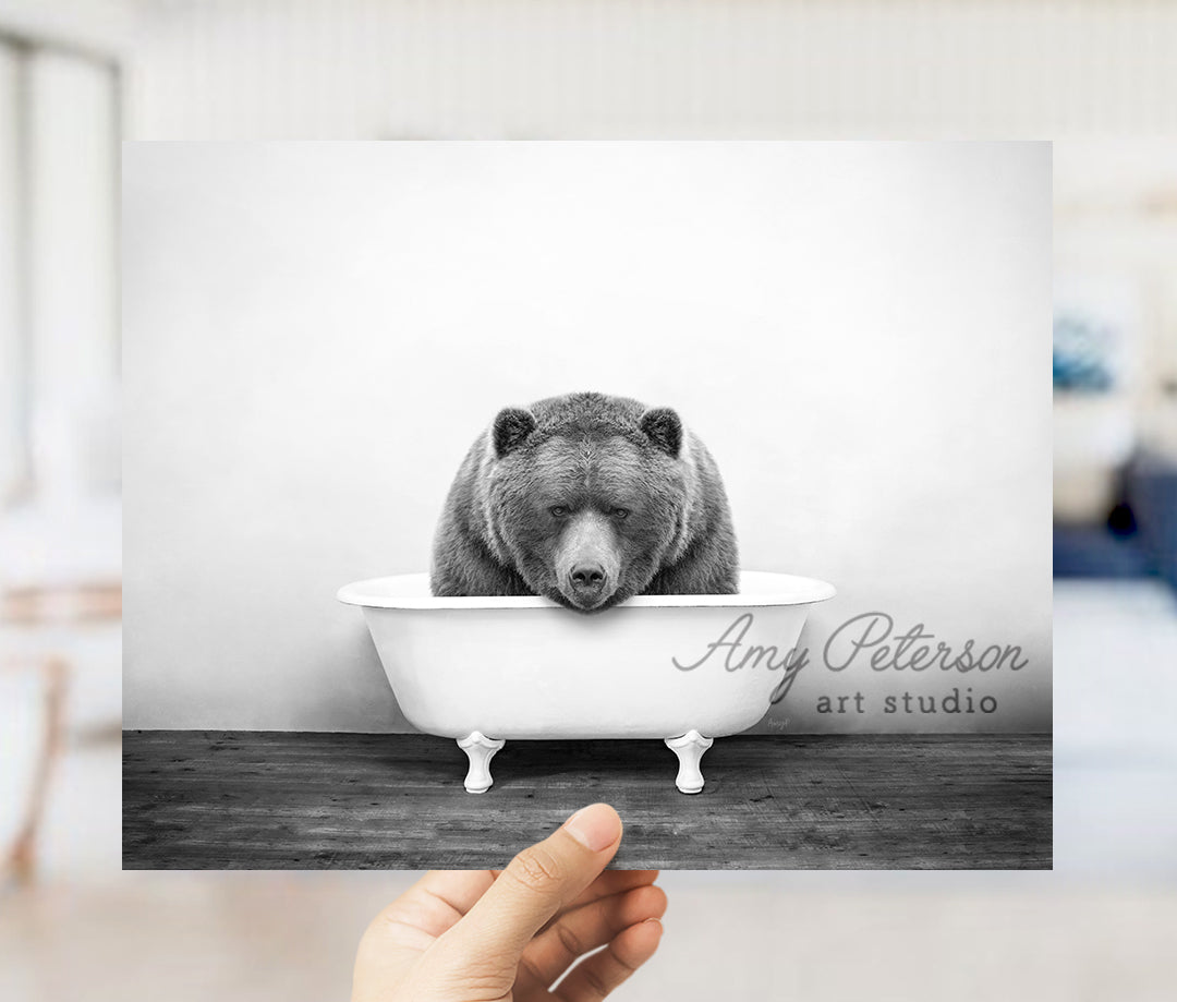 a hand holding up a black and white photo of a bear in a bathtub