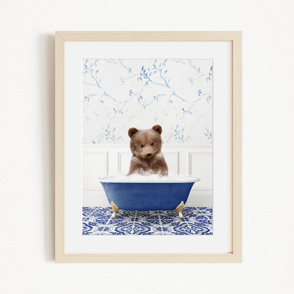 A small brown bear is sitting in a blue bathtub filled with water, surrounded by a blue and white patterned rug on the floor.