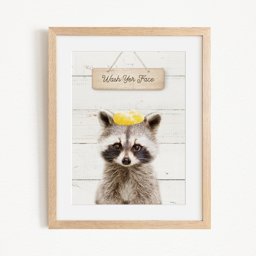 A raccoon wearing a yellow hat with the text "Wash Your Face" written on it, set against a white wooden background.