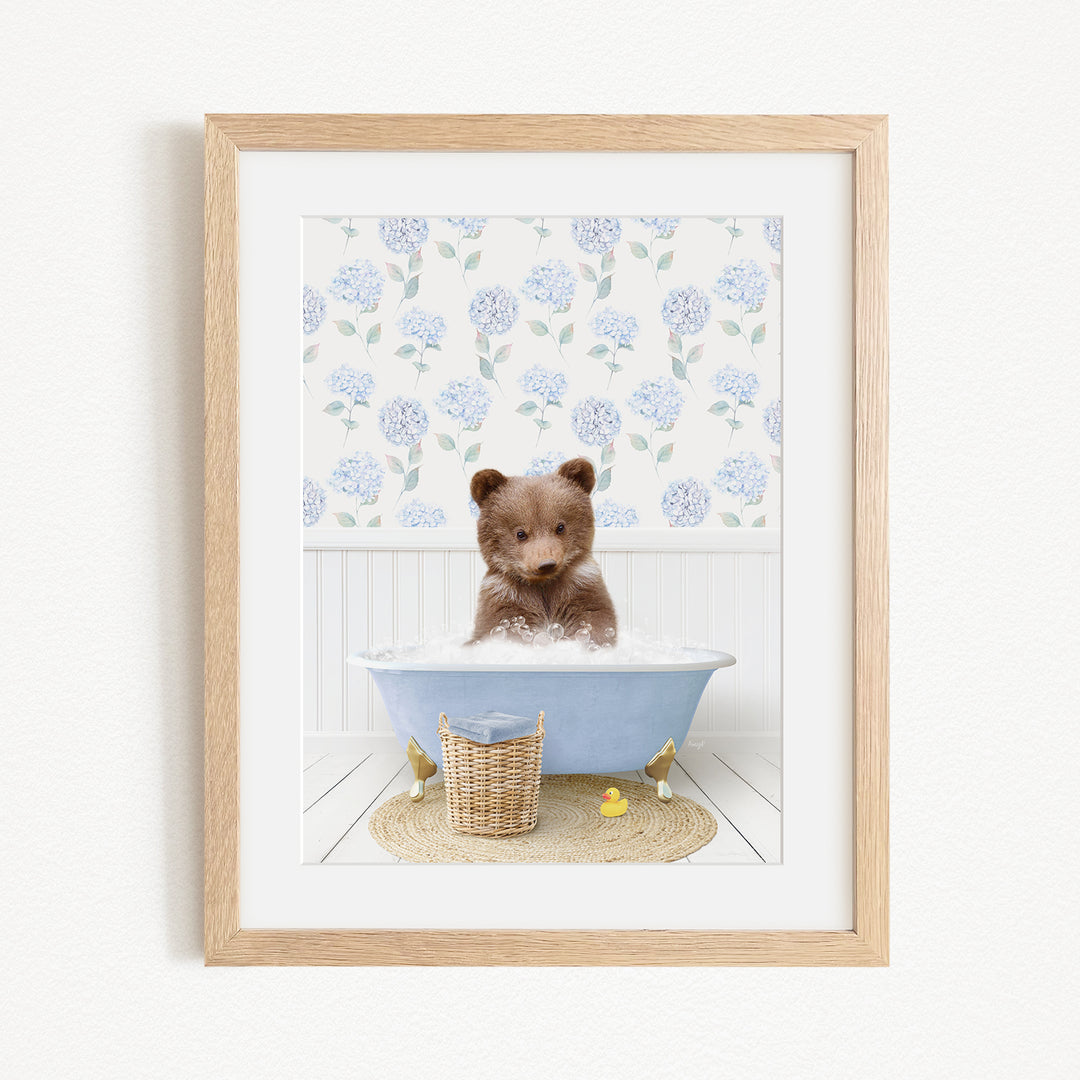 A brown bear sitting in a blue bathtub filled with bubbles, surrounded by a floral patterned wall and a basket of rubber ducks.