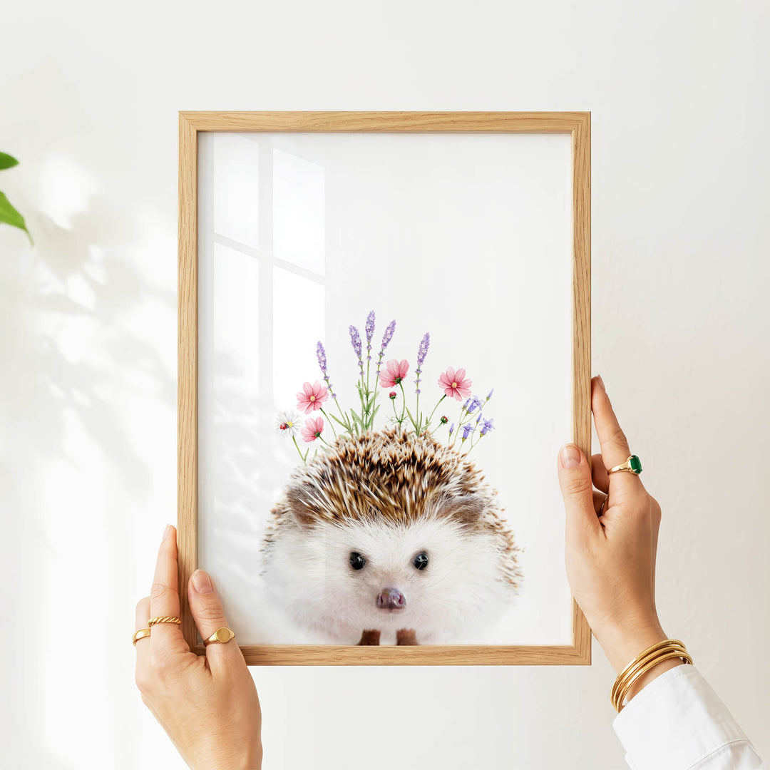 A person's hands are holding a wooden frame with a picture of a hedgehog wearing a floral crown.