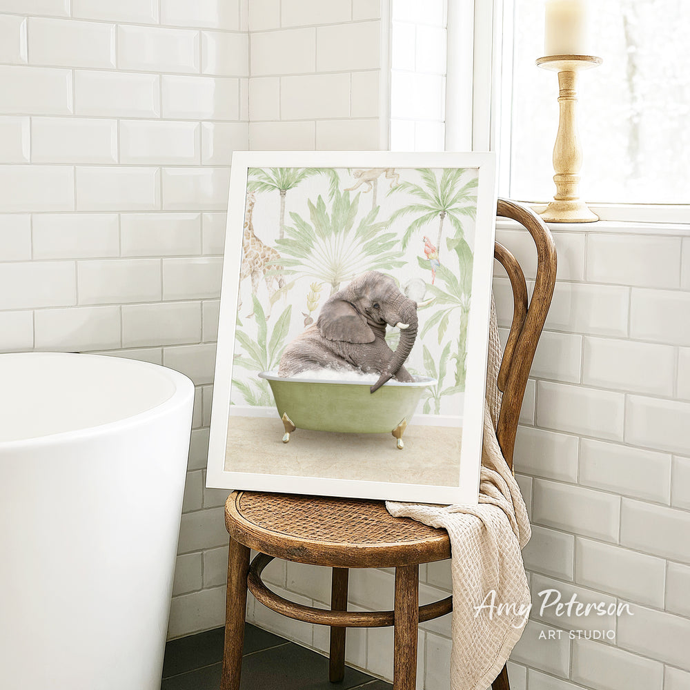 A framed image of a gray elephant sitting in a green bathtub, surrounded by tropical foliage, is displayed on a wooden chair in a bathroom setting.