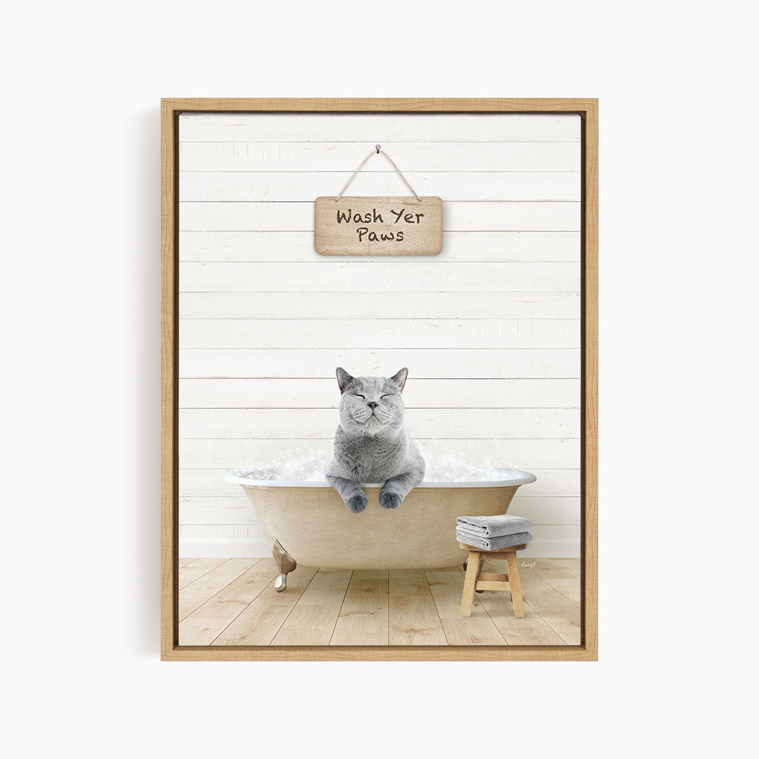 A gray cat sitting in a bathtub filled with bubbles, with a wooden sign above that says "Wash Your Paws".