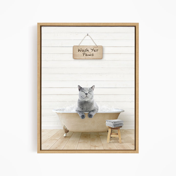 A gray cat sitting in a bathtub filled with bubbles, with a wooden sign above that says "Wash Your Paws".