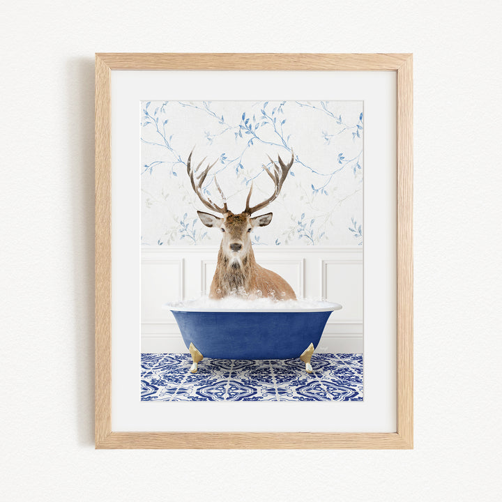 A deer with large antlers is sitting in a blue bathtub, surrounded by a patterned tile floor and a white wall with blue floral wallpaper.