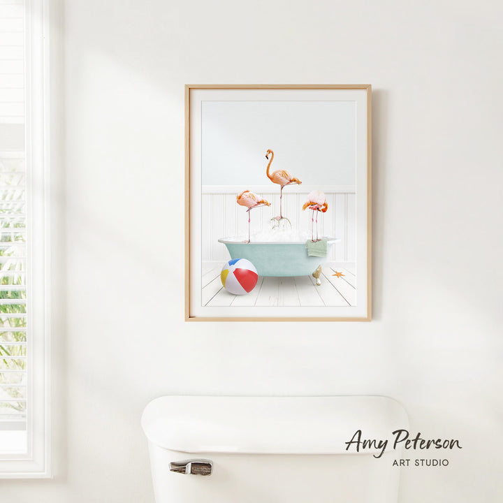 A framed print of a vibrant, colorful scene depicting a bathtub filled with three flamingos, a beach ball, and a towel, hanging on a white wall.
