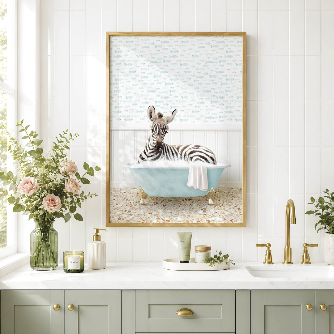 A framed image of a zebra sitting in a bathtub, surrounded by flowers and a decorative vase, is displayed on a white tiled wall above a bathroom sink.