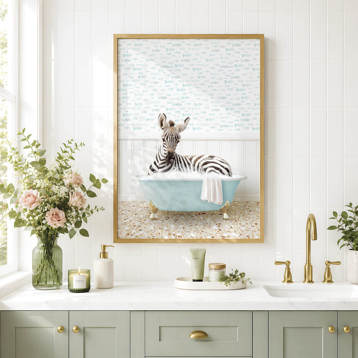A framed image of a zebra sitting in a bathtub, surrounded by flowers and a decorative vase, is displayed on a white tiled wall above a bathroom sink.