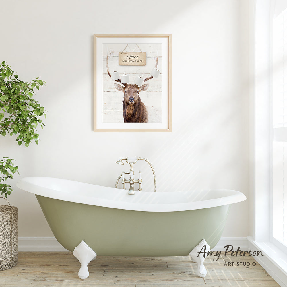 a green clawfoot bathtub with a framed picture of a deer above it, set against a white wall and wooden floor.
