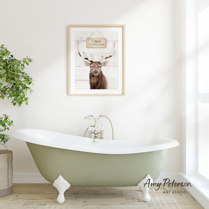 a green clawfoot bathtub with a framed picture of a deer above it, set against a white wall and wooden floor.