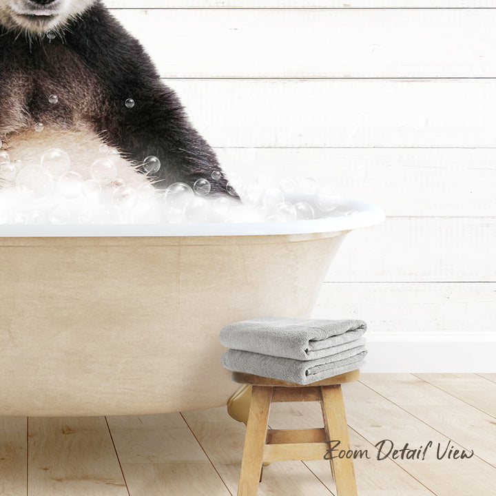 A panda resting in a bathtub filled with bubbles, with a towel and stool nearby.