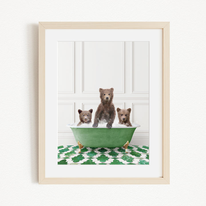 A framed image depicting three brown bears sitting in a green bathtub, with a patterned green and white rug on the floor beneath them.