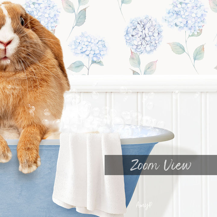 A brown rabbit sitting in a blue bathtub filled with bubbles, with a towel and a floral patterned wall in the background.