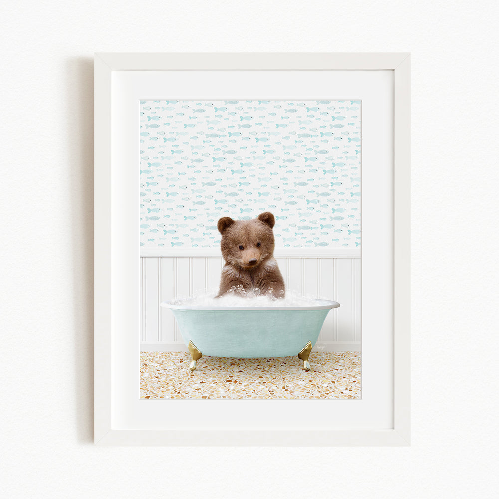 A small brown bear sitting in a light blue bathtub filled with bubbles, surrounded by a patterned wall and a beige and white tiled floor.
