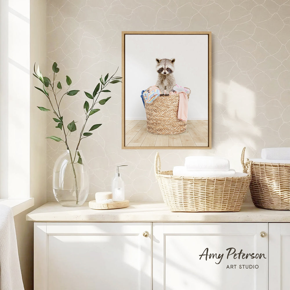 a framed photograph of a raccoon sitting in a woven basket, placed on a wall above a white cabinet.