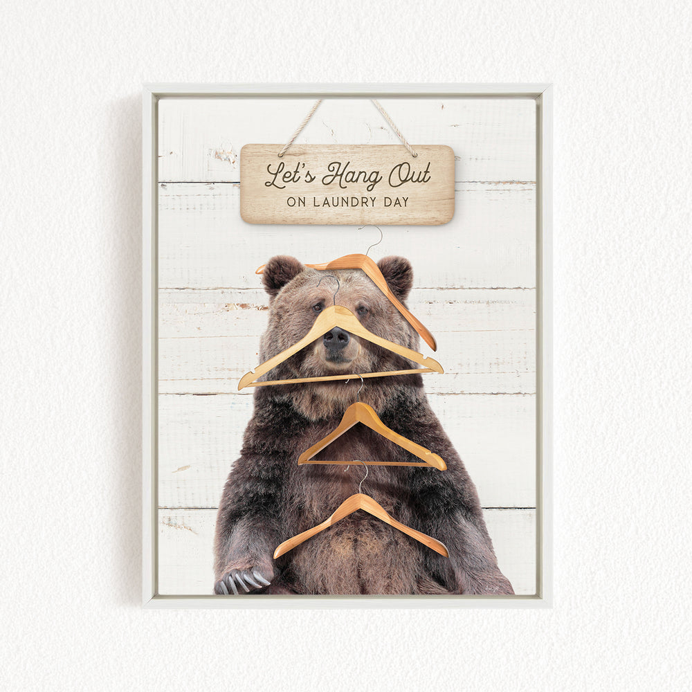 A wooden sign with the text "Let's Hang Out on Laundry Day" hangs above a large bear sitting on a wooden surface.