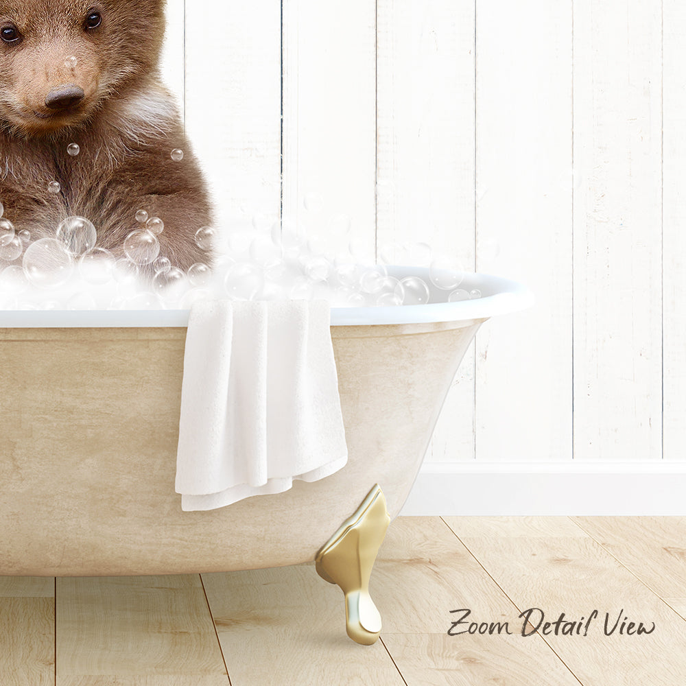 A brown bear sitting in a white bathtub filled with bubbles, with a towel and gold bathtub leg visible.