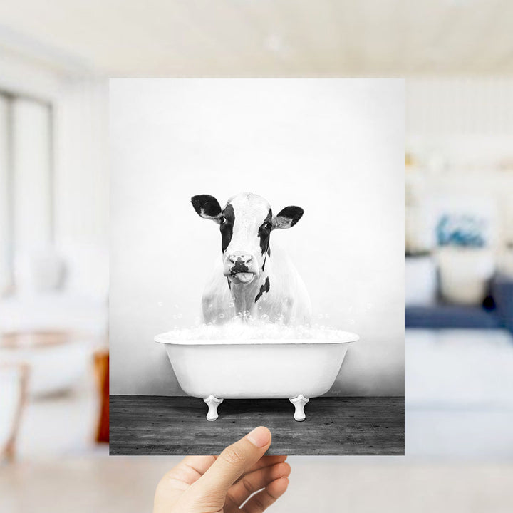 A black and white photograph of a cow sitting in a bathtub filled with water, with a blurred background suggesting a living room setting.