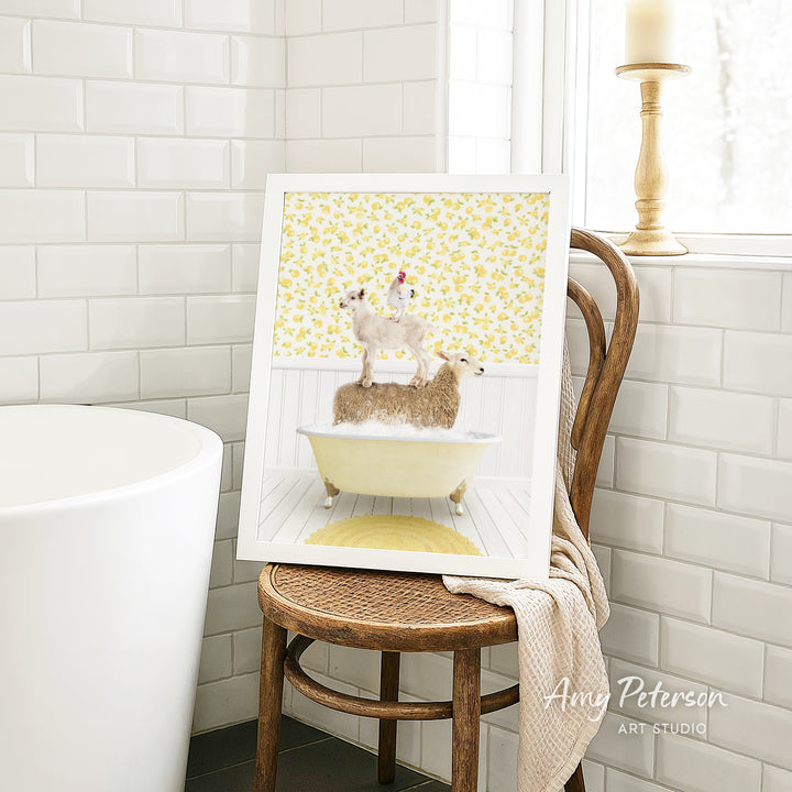 A framed image of a cat sitting on a yellow bathtub, with a sheep on top, is displayed on a wooden chair in a bathroom setting.