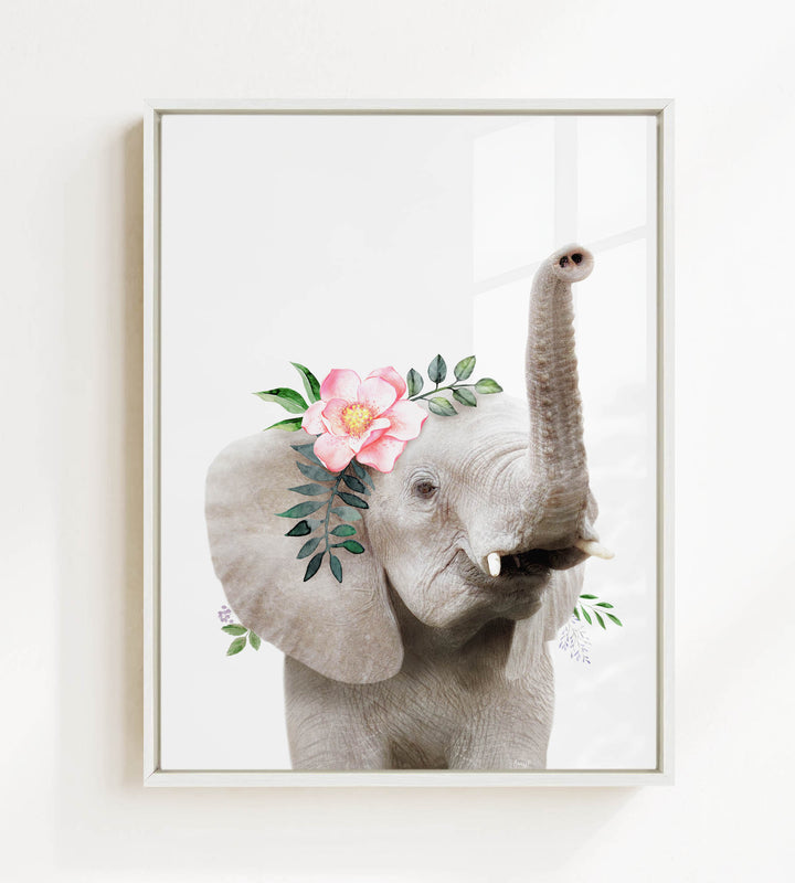 A framed image of an elephant with a pink flower and green leaves adorning its head.