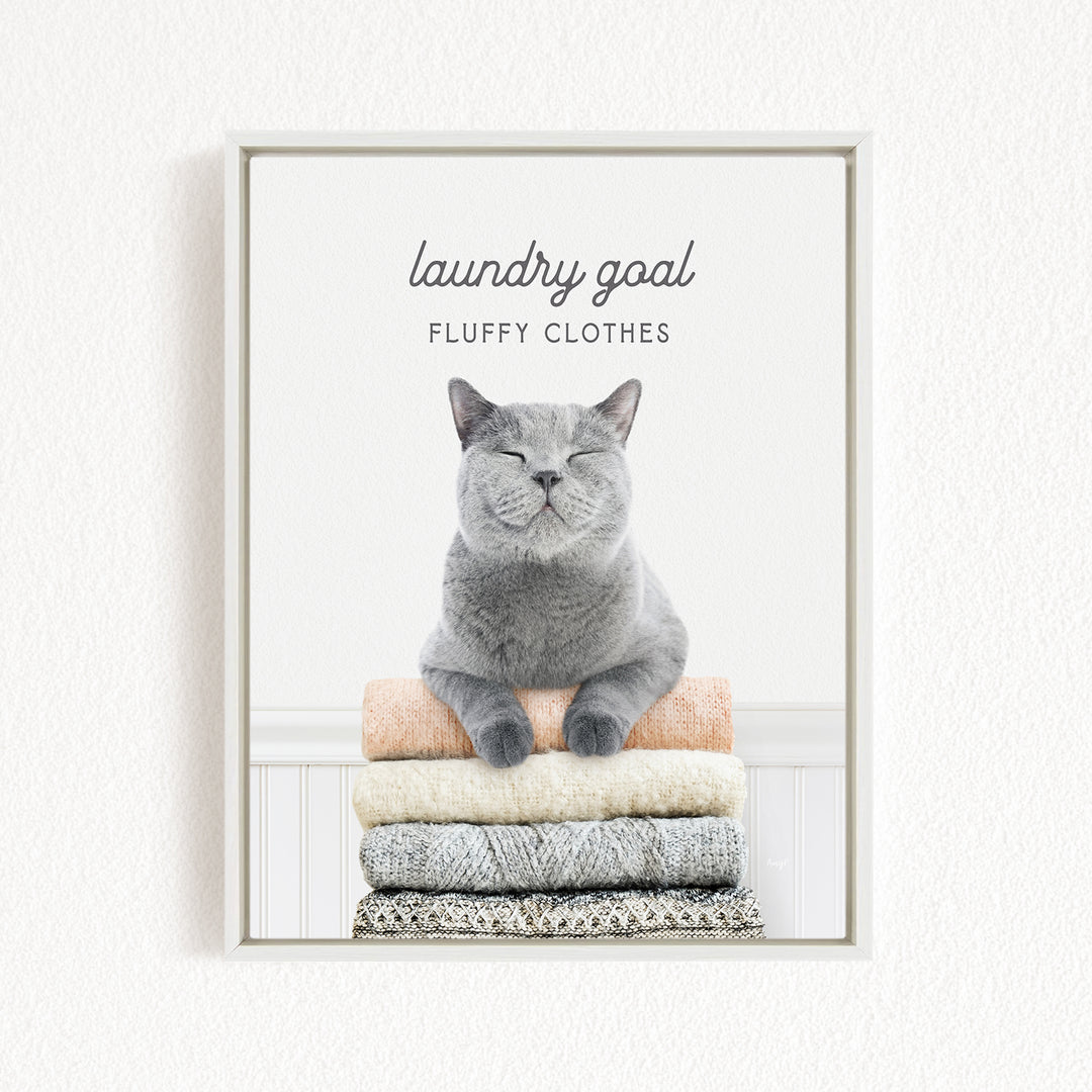 A gray cat sitting on a stack of clothes, with the text "laundry goal" and "fluffy clothes" above it.