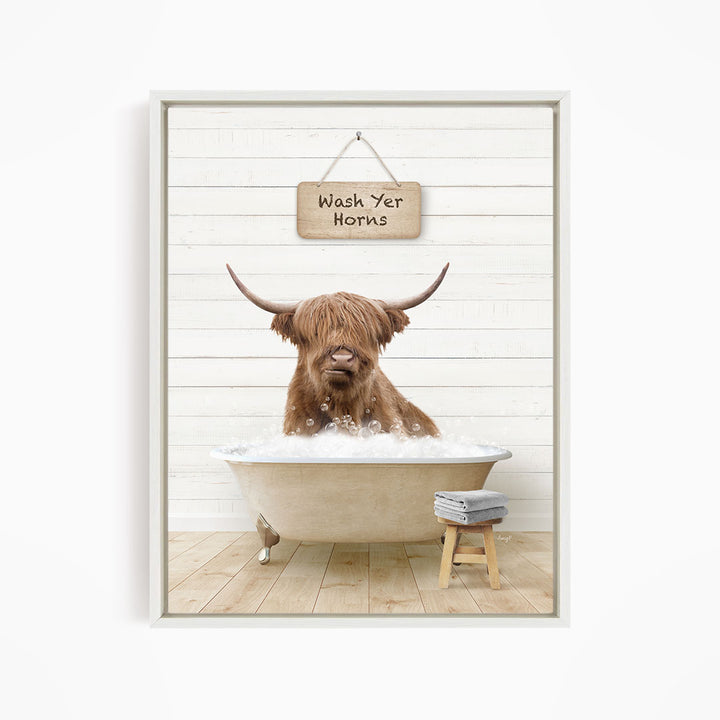 A brown cow with long horns is sitting in a bathtub filled with bubbles, with a sign above that says "Wash Yer Horns".