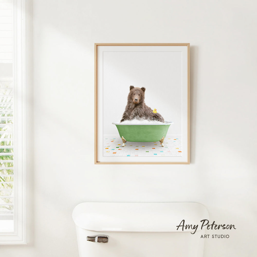 A framed image of a brown bear sitting in a green bathtub, surrounded by colorful tiles, is displayed on a white wall.
