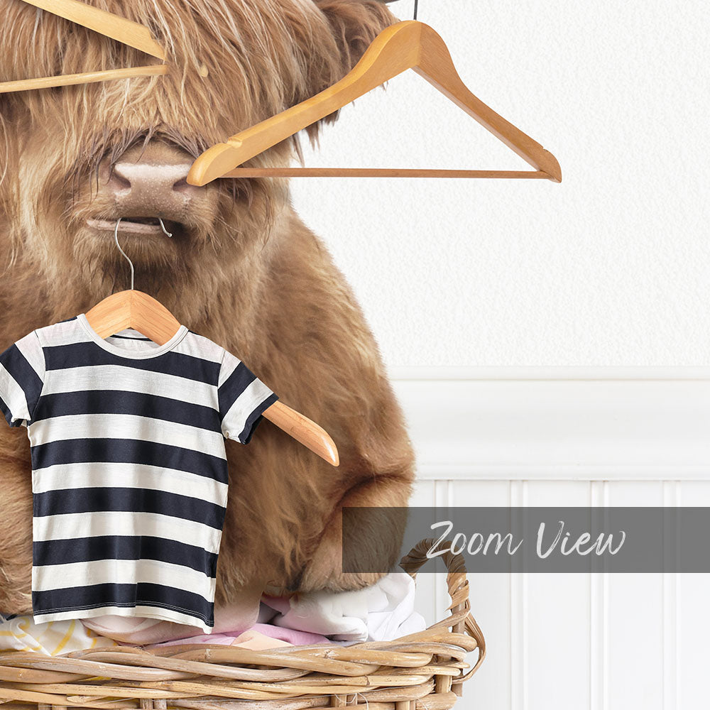 A large, furry animal resembling a yak or a similar creature is sitting on a clothesline, holding a striped shirt on its back.