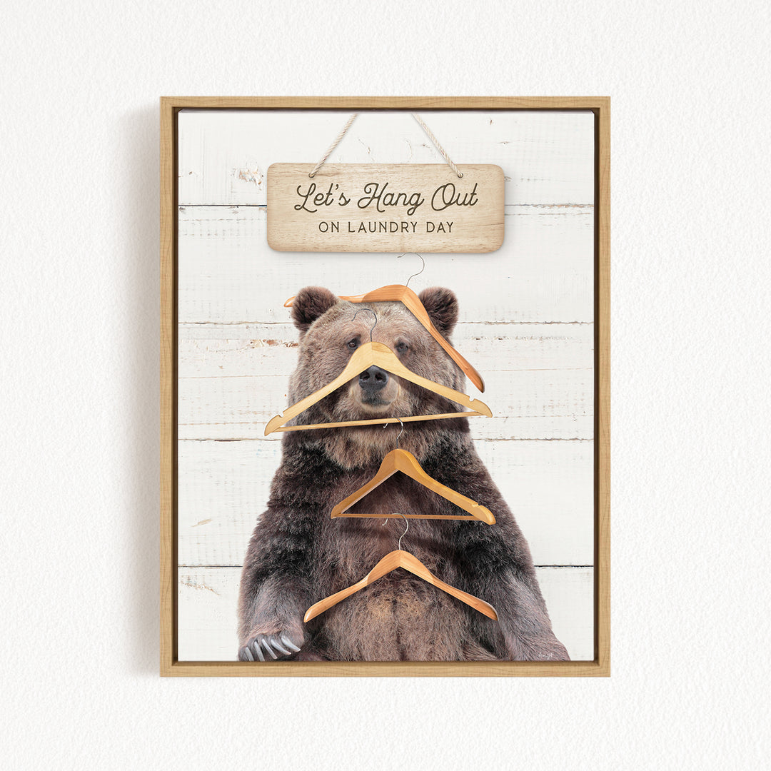 A framed image of a bear sitting on a wooden surface, with a sign above it that says "Let's Hang Out on Laundry Day".