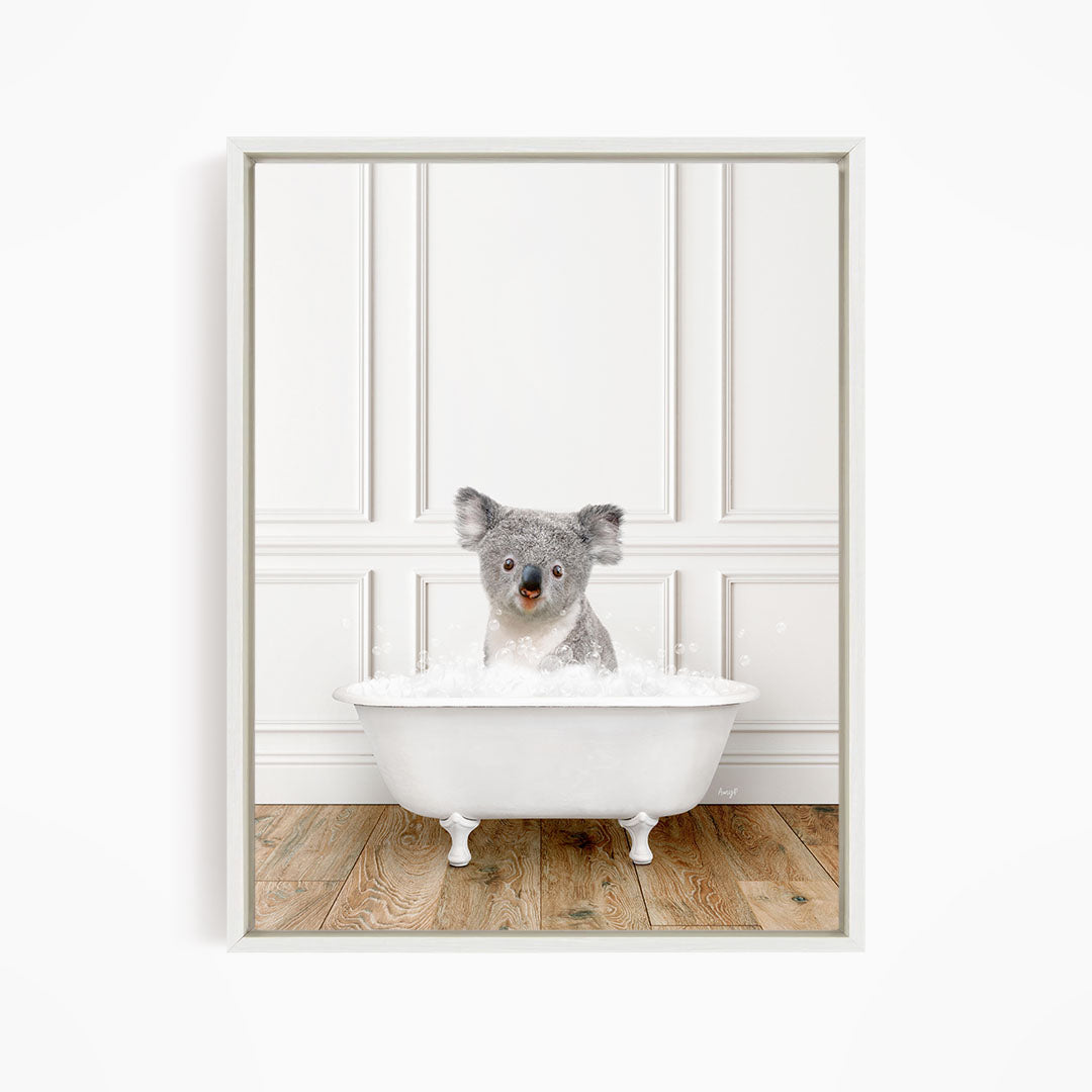 A koala bear sitting in a white bathtub filled with bubbles, looking directly at the camera.