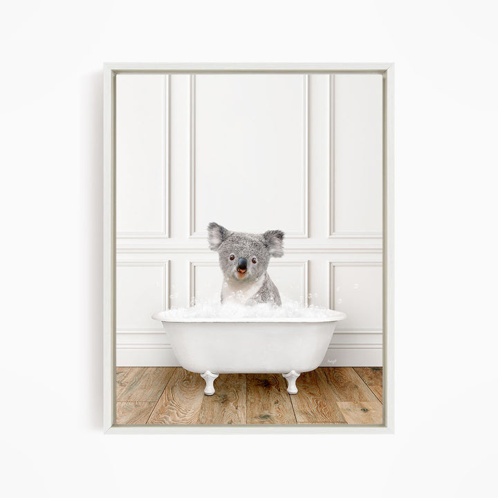 A koala bear sitting in a white bathtub filled with bubbles, looking directly at the camera.