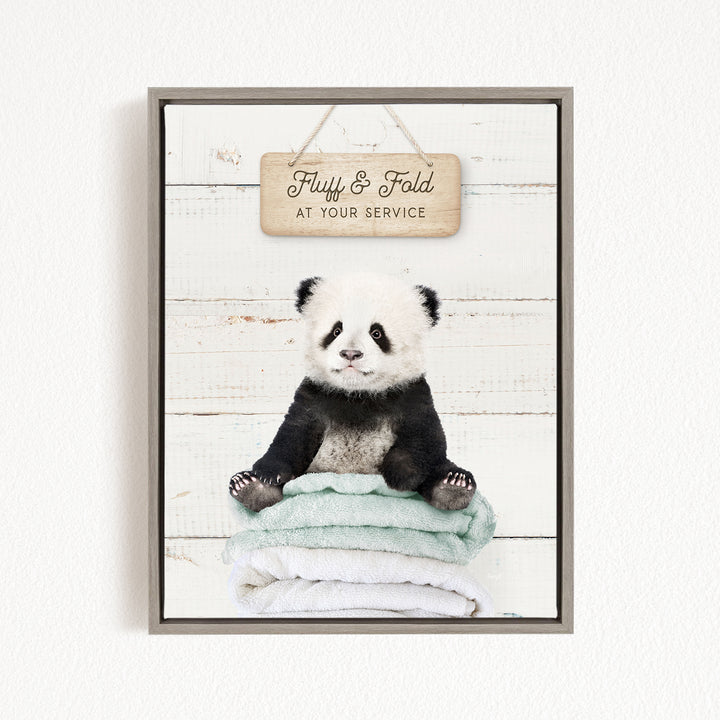 A panda bear sitting on a stack of towels, with a wooden sign above that says "Fluffy & Fold at your Service".