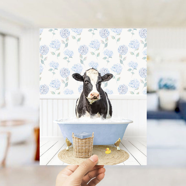A black and white cow is sitting in a blue bathtub filled with water, surrounded by a floral patterned wall.