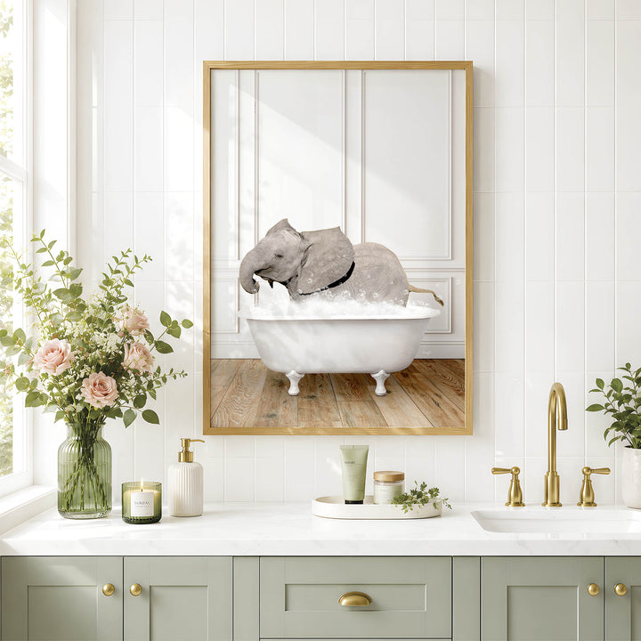 A framed image of a gray elephant sitting in a white bathtub, surrounded by pink flowers, is displayed on a white tiled wall above a white countertop with various bathroom accessories.