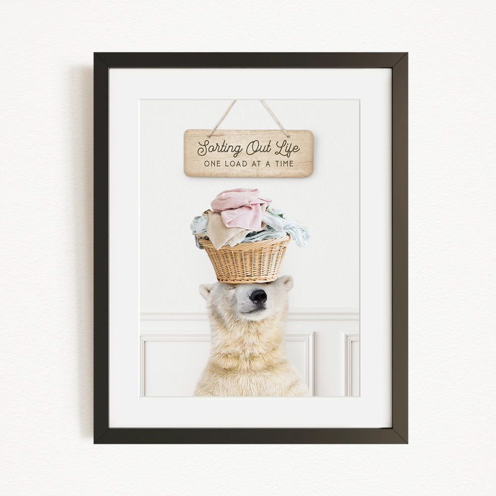 A polar bear balancing a basket of laundry on its head, with a sign above that reads "Sorting Out Life One Load at a Time".