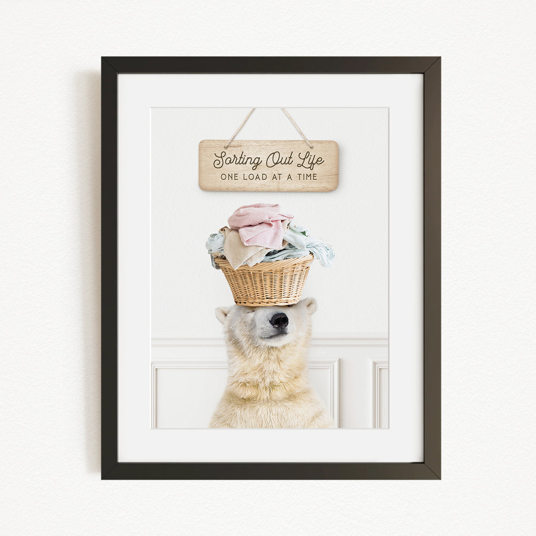 A polar bear balancing a basket of laundry on its head, with a sign above that reads "Sorting Out Life One Load at a Time".