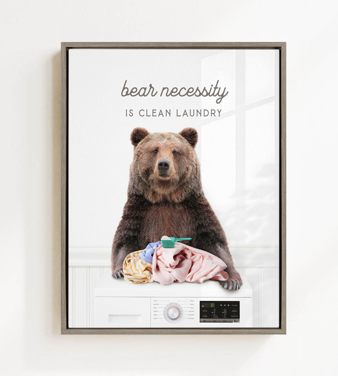 A brown bear sitting on a washing machine, with clothes and a toothbrush nearby, and the text "bear necessity is clean laundry" above the bear.