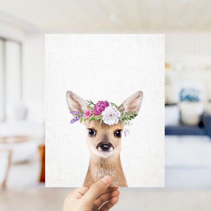 A hand is holding up a framed print of a deer wearing a floral crown.