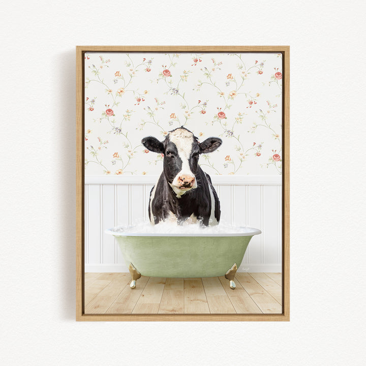 A black and white cow is sitting in a green bathtub filled with water, surrounded by a floral wallpaper.