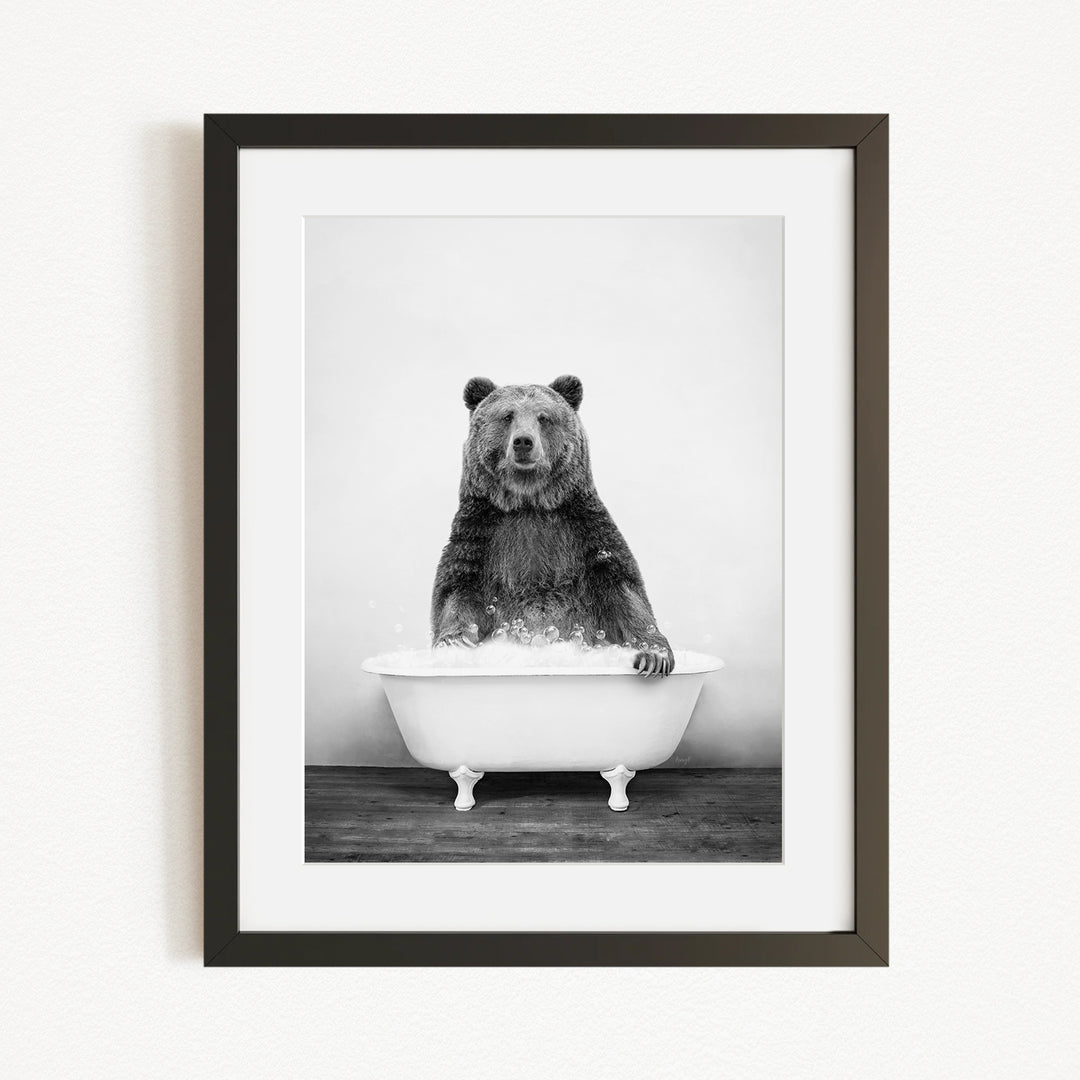 A black and white photograph of a bear sitting in a bathtub filled with water.