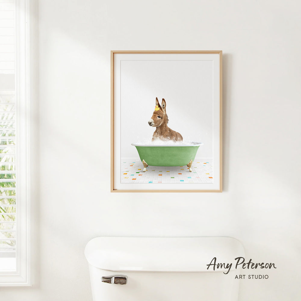 A framed print of a donkey sitting in a green bathtub, with a white toilet in the foreground.