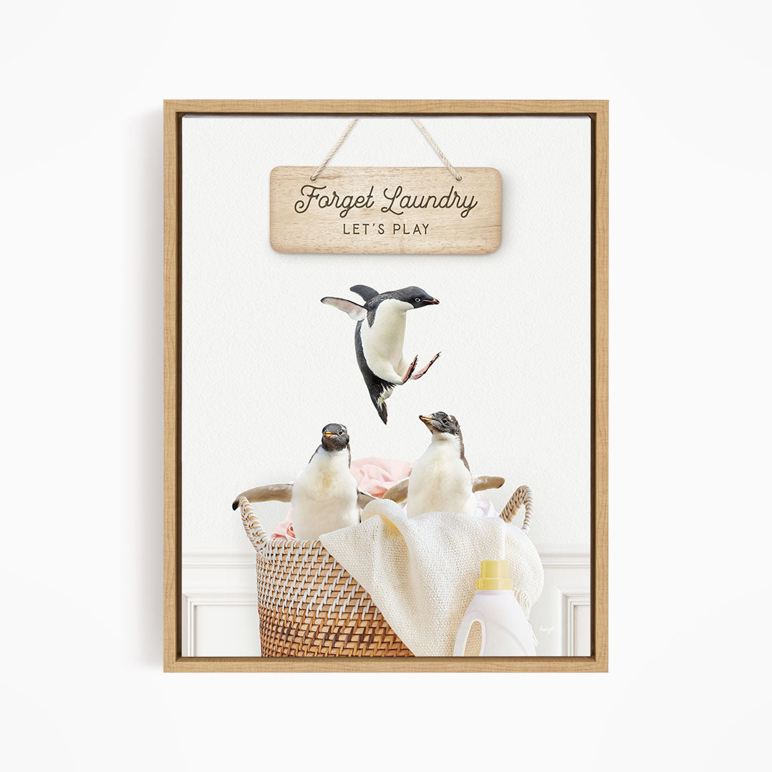 A framed image depicting three penguins in a basket, with a sign above that says "Forget Laundry, Let's Play".