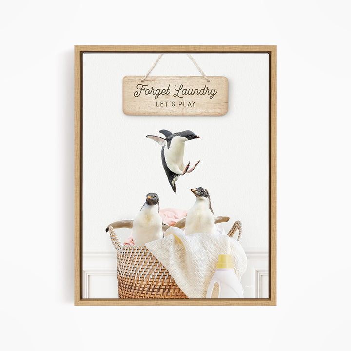A framed image depicting three penguins in a basket, with a sign above that says "Forget Laundry, Let's Play".