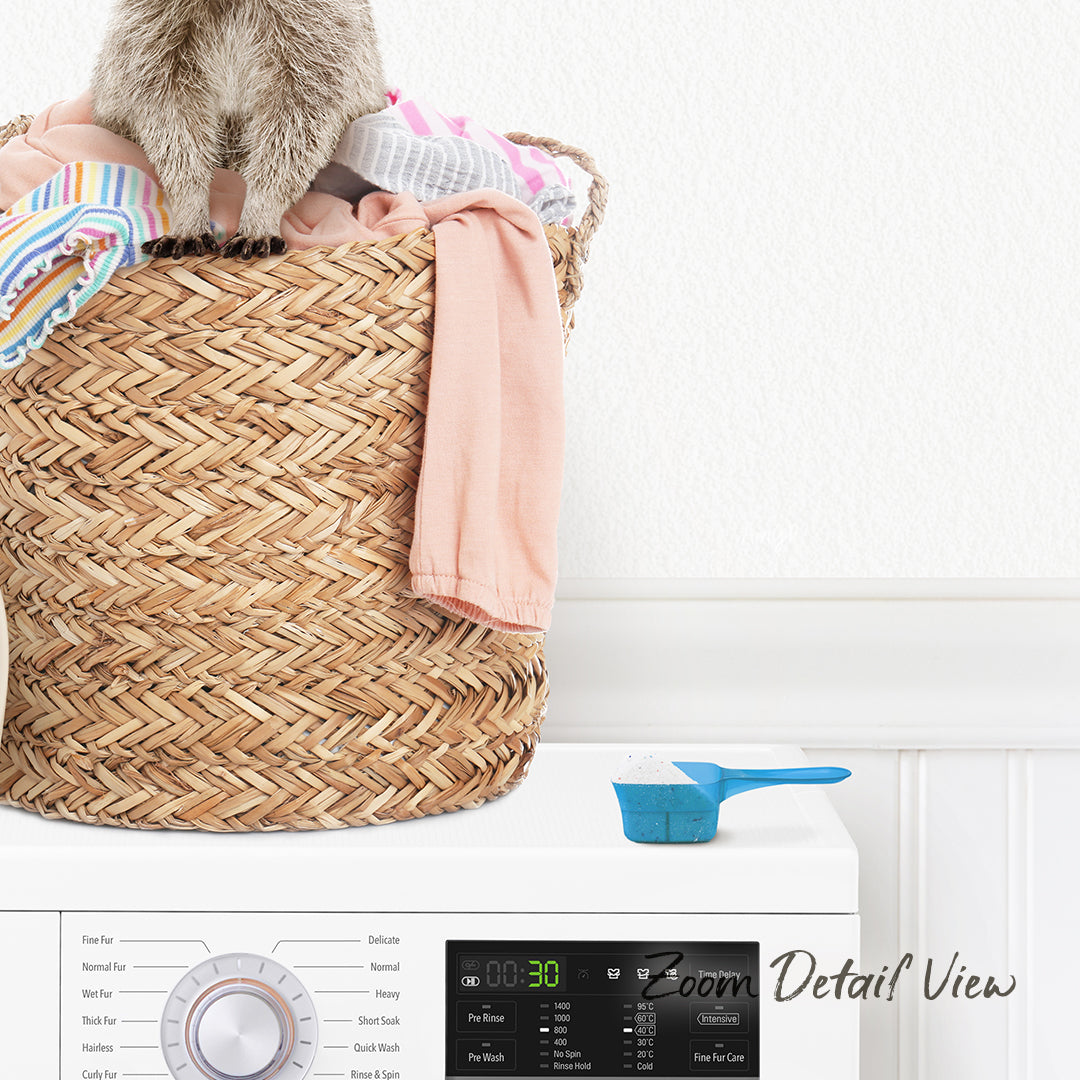 A laundry basket filled with clothes sits on top of a washing machine, with a small blue measuring cup placed on the front of the machine.