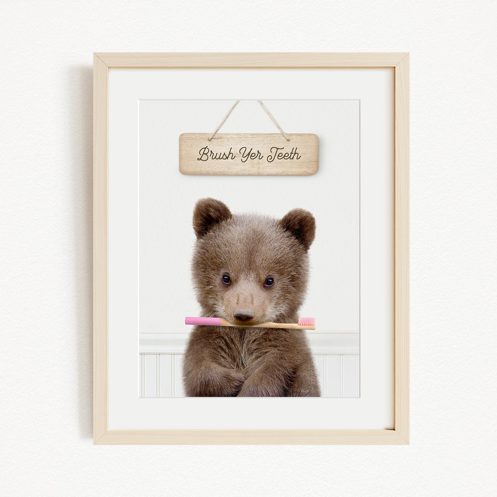 A cute brown bear cub holding a pink toothbrush, with a wooden sign above that says "Brush Your Teeth".