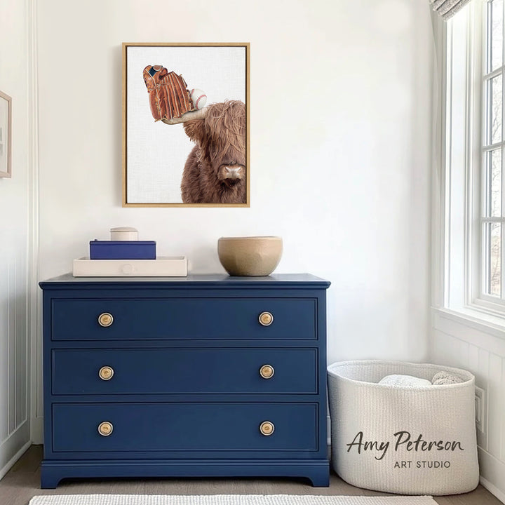 a blue dresser with a framed picture of a brown cow on it, along with a white basket and a small bowl on top of the dresser. The dresser is situated in a room with a window and a white wall.