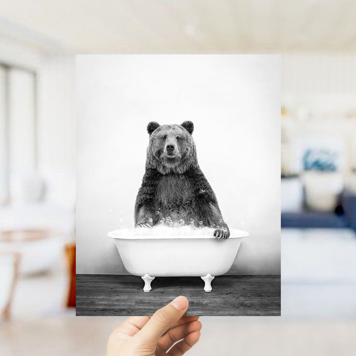 A hand holds up a black and white photograph of a bear sitting in a bathtub filled with water.