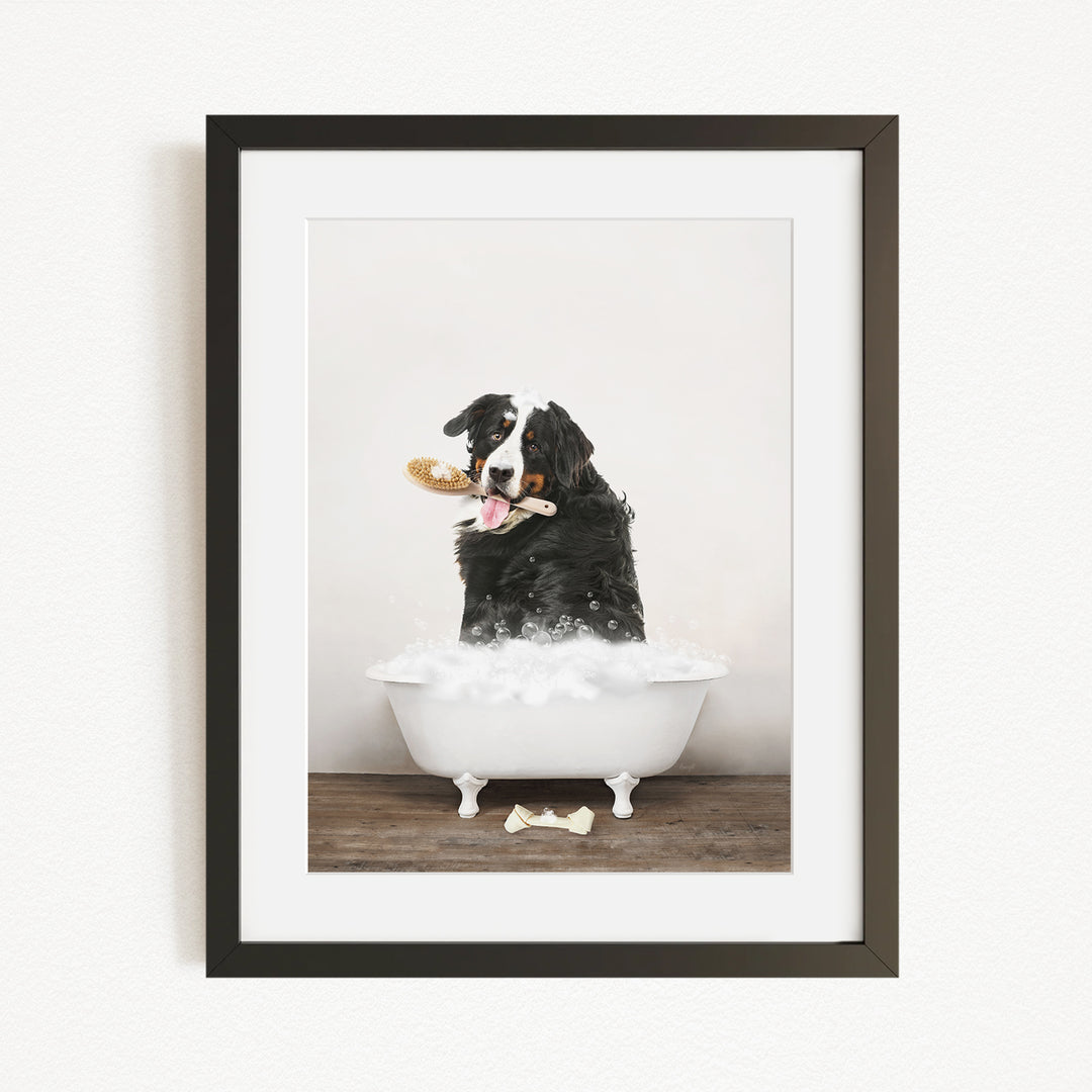 A black and white dog sitting in a white bathtub, holding a toy in its mouth, with a white bone on the floor.
