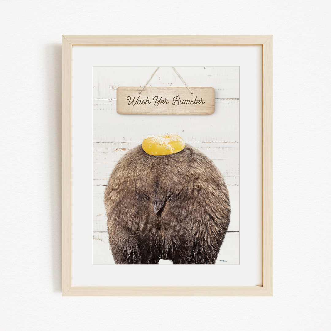 A framed image of a bear with a yellow object on its head, accompanied by a wooden sign that says "Wash Your Bummer".